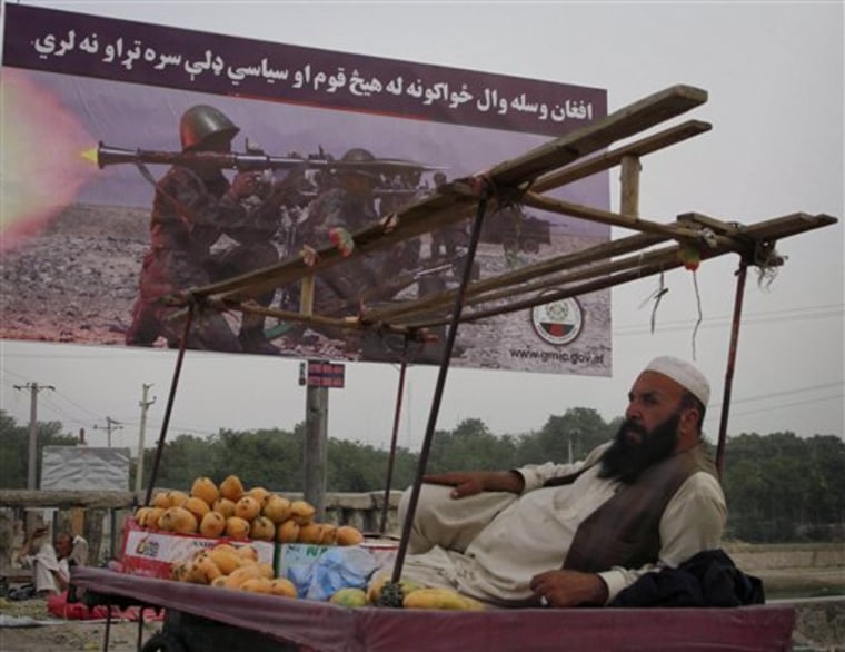 An Afghan man selling mangos waits for costumers, as a military billboard is seen in the background reading\" The Afghan soldiers has no related to any ethnic and political groups\" in Kabul, Afghanistan on Sunday, June. 26, 2011. (AP Photo/Ahmad Nazar)